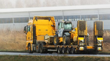 Construction equipment haulage. Excavators and cranes are on transportation truck with long trailer platform on the highway.